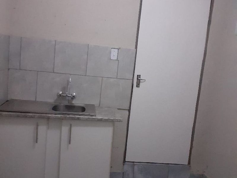 A compact kitchen area featuring a single sink, base cabinetry with laminate countertop, tiled splashback, and tiled flooring.