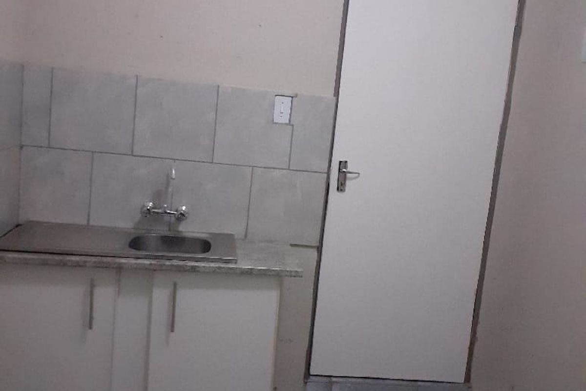 A compact kitchen area featuring a single sink, base cabinetry with laminate countertop, tiled splashback, and tiled flooring.