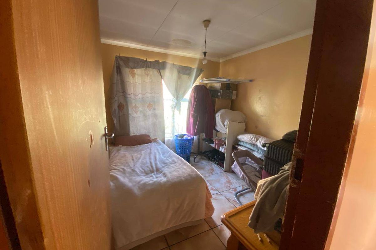 A compact bedroom featuring tiled flooring and a central ceiling light fixture, currently used as a functional living space.