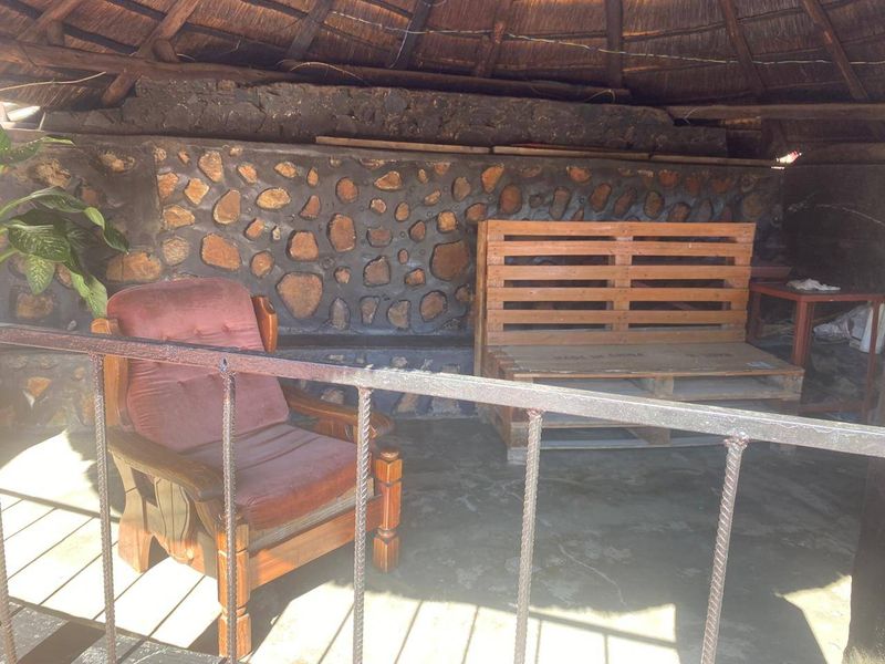 Outdoor covered patio area featuring a rustic thatched roof, stone-clad feature wall, and metal safety railing.