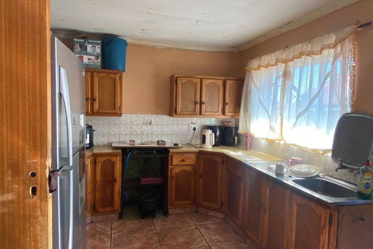 A dated kitchen featuring wooden cabinetry, tiled backsplash, and tiled flooring, offering significant potential for modernization and renovation.