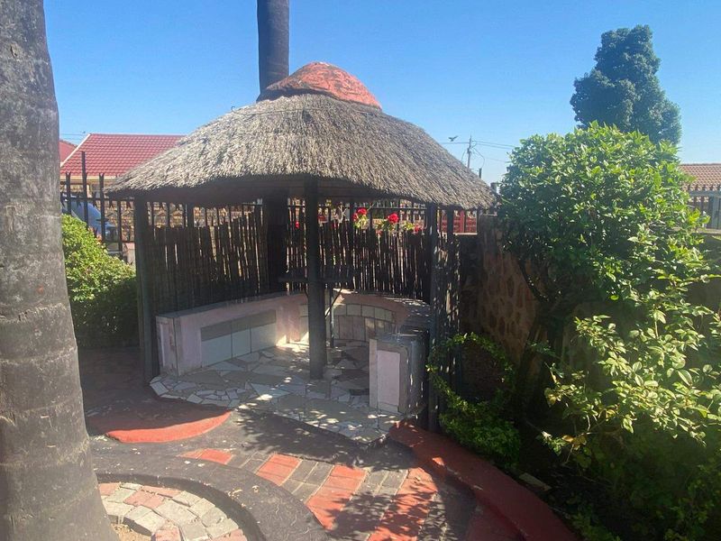 Outdoor thatched lapa area featuring built-in seating and a mix of stone and brick paving, ideal for garden entertainment.