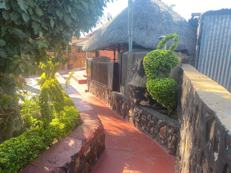 A garden pathway featuring a thatched roof structure, stone retaining walls, and established landscaping.