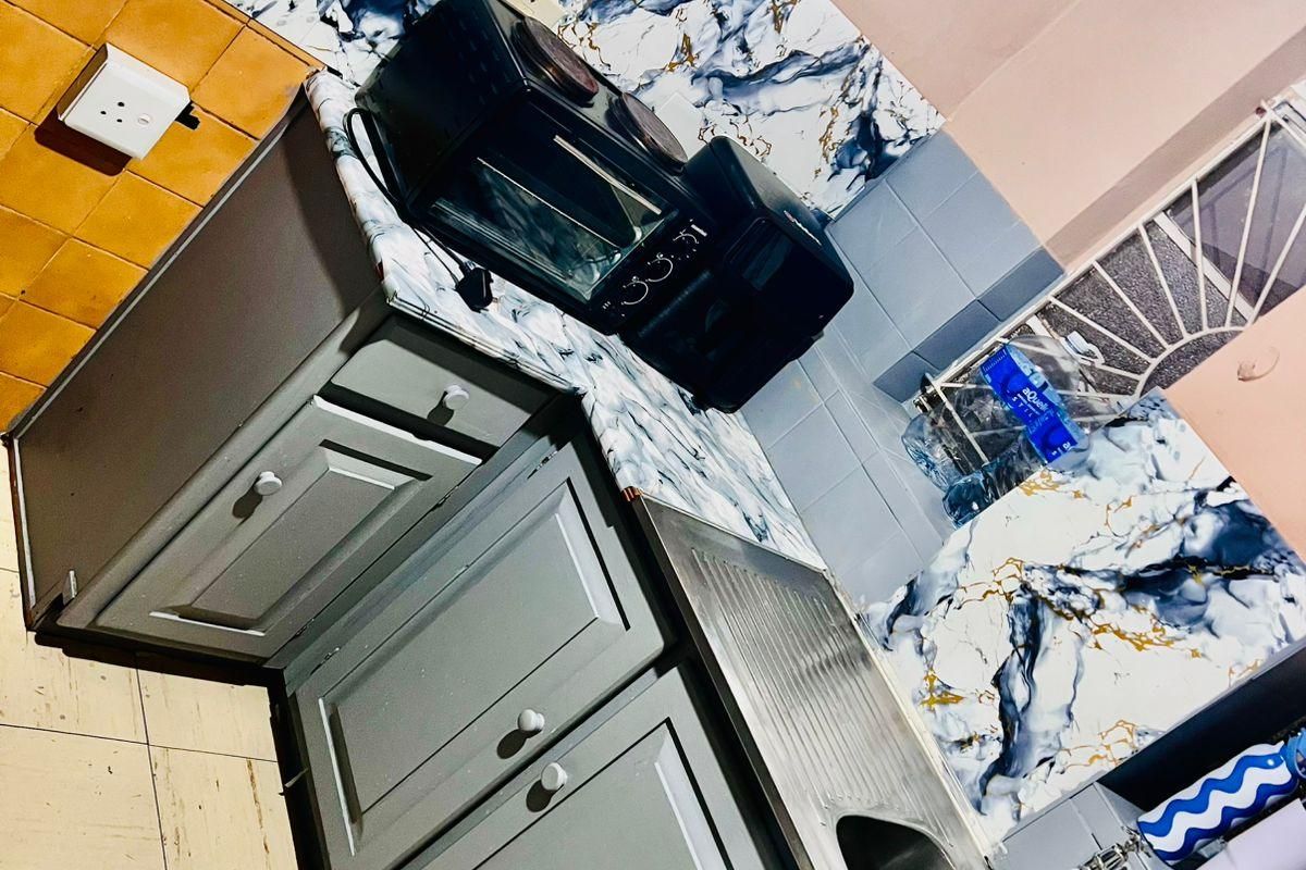 A compact kitchen area featuring grey cabinetry, a stainless steel sink, and a distinctive marble-effect splashback with mixed wall tiling.