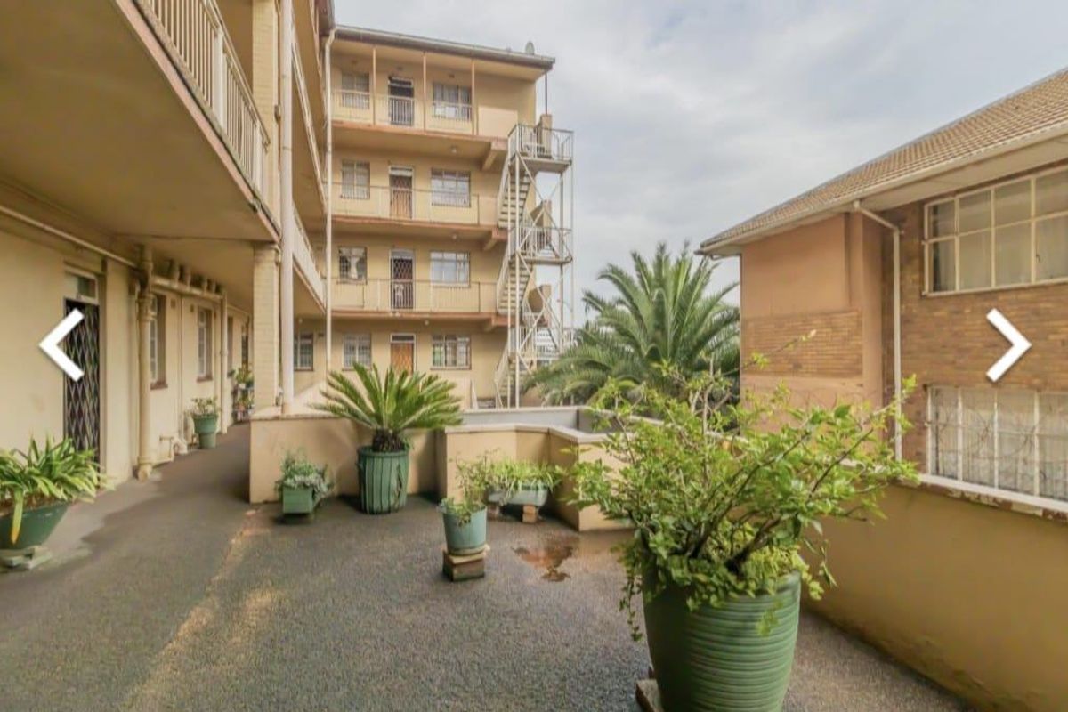 View of the apartment complex rear exterior, featuring paved communal areas, external staircases, and multi-story brick building facades.