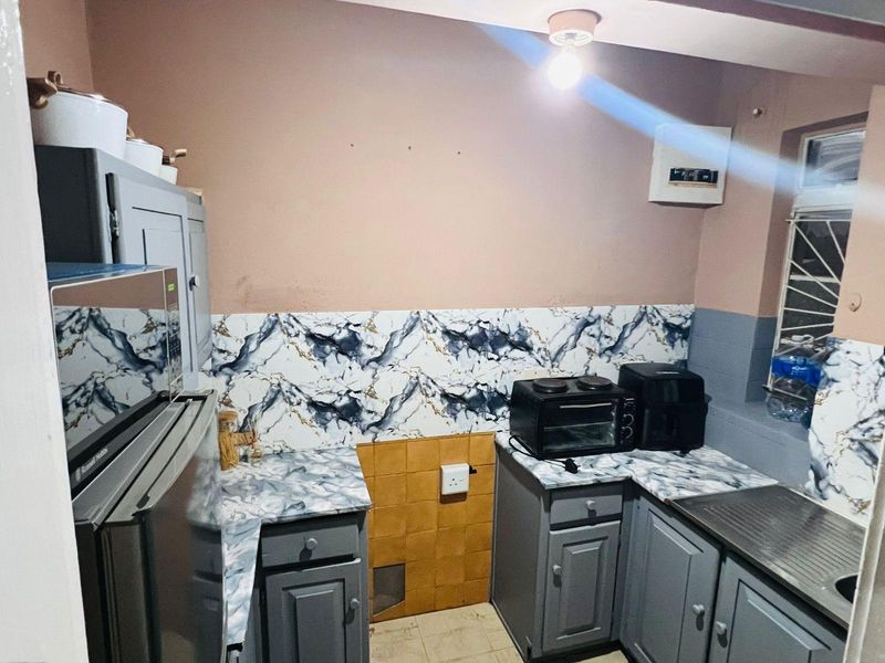 Compact kitchen featuring grey cabinetry, marble-effect countertops, and a stainless steel sink, requiring cosmetic updates to improve the overall finish and aesthetic appeal.