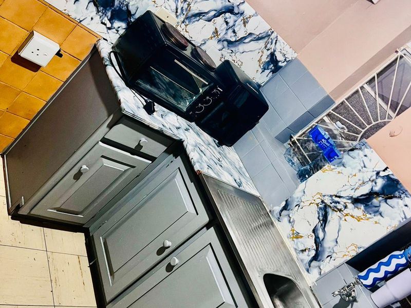 A compact kitchen area featuring grey cabinetry, a stainless steel sink, and a distinctive marble-effect splashback with mixed wall tiling.