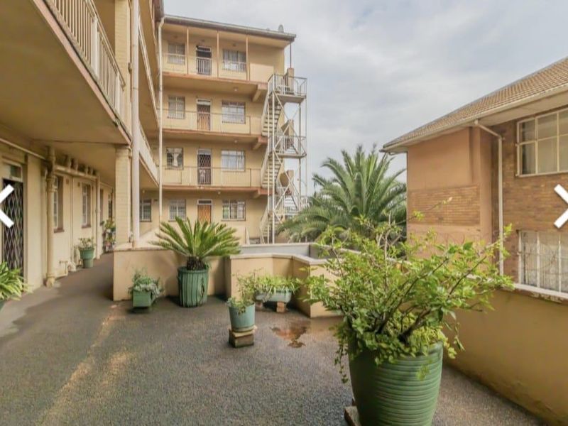 View of the apartment complex rear exterior, featuring paved communal areas, external staircases, and multi-story brick building facades.
