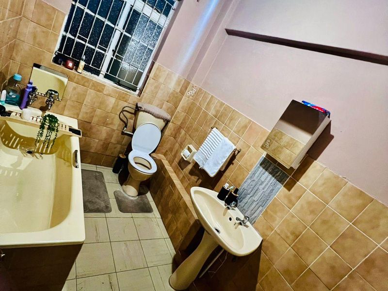 A dated bathroom featuring a pedestal basin, bathtub, and toilet with tiled finishes and security bars on the window.