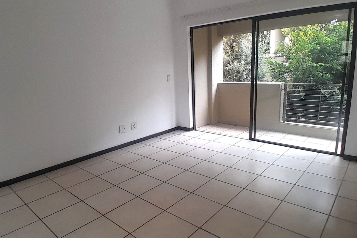 An empty, neutrally finished living area featuring tiled flooring and a large sliding glass door providing access to an outdoor balcony.