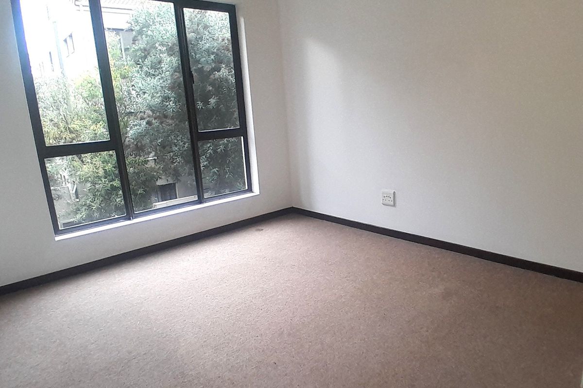 An empty bedroom featuring neutral walls, carpet flooring, and a large window providing natural light and a view of the surrounding greenery.