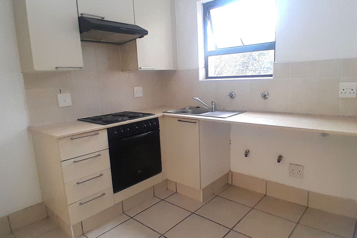 A functional kitchen featuring built-in cabinetry, an electric stove with extractor fan, stainless steel sink, and tiled flooring.