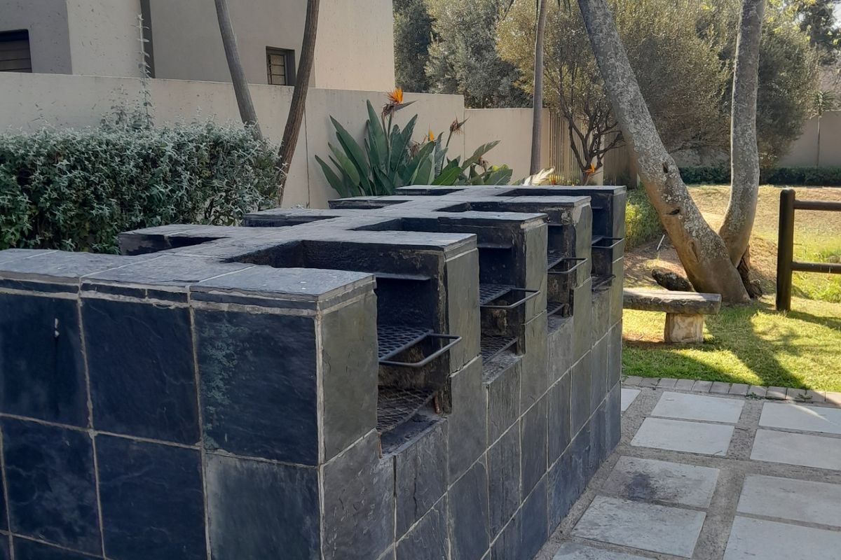 Outdoor entertainment area featuring a large built-in stone-tiled braai station set on a paved patio within a garden setting.