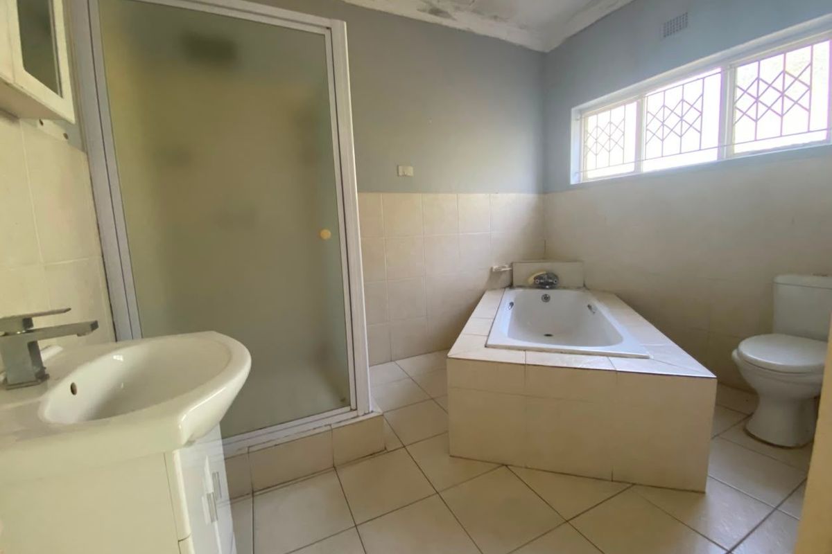 A spacious bathroom featuring a built-in bathtub, separate shower enclosure, pedestal basin, and toilet, with tiled finishes throughout.