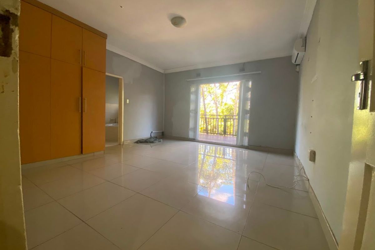 Spacious bedroom featuring tiled flooring, built-in cupboards, an air conditioning unit, and direct access to a private balcony.