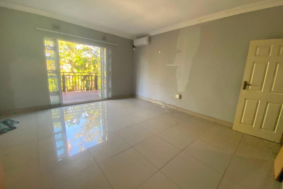 An empty living room featuring tiled floors, a wall-mounted air conditioner, and sliding glass doors leading to an outdoor balcony.