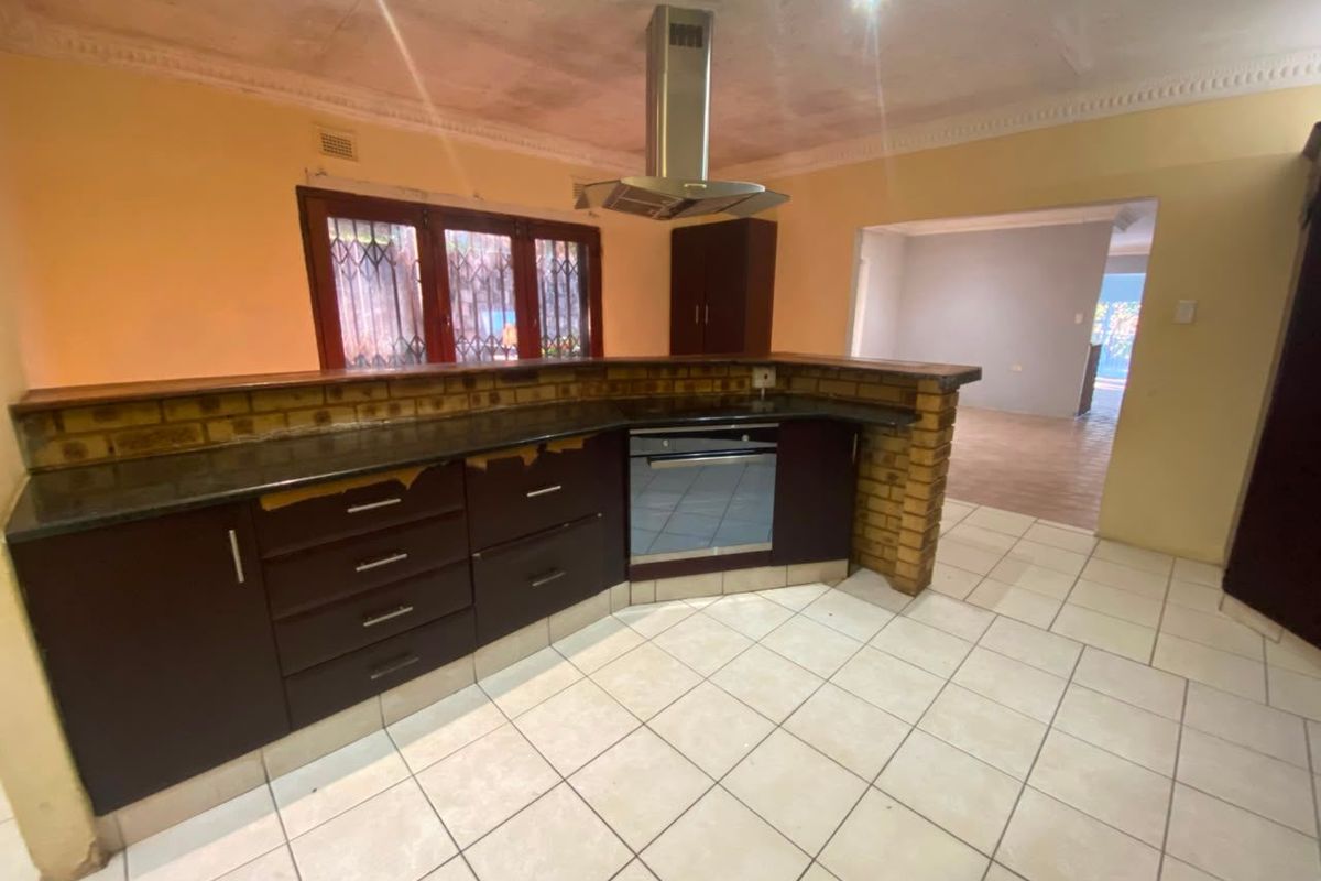Kitchen featuring dark cabinetry, granite countertops, a brick breakfast bar, and built-in oven with extractor fan. Requires cosmetic updates to ceiling and cabinetry.
