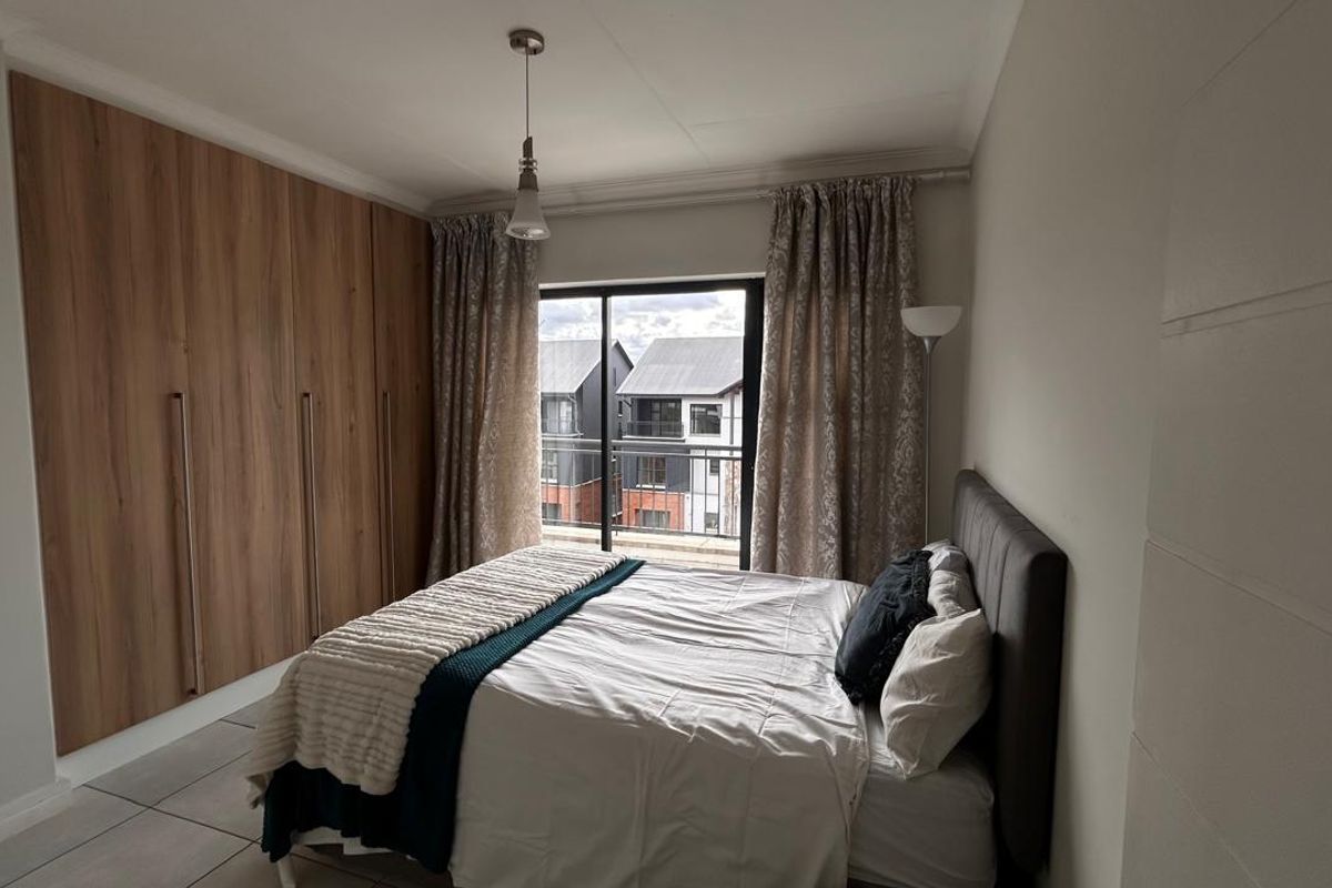 A well-maintained bedroom featuring modern wood-finish built-in cupboards, tiled flooring, and a sliding door providing access to a private balcony.
