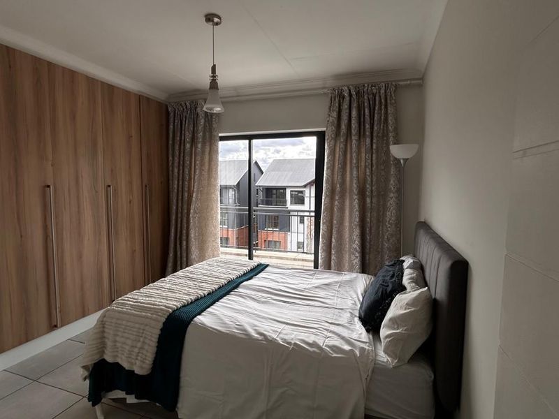 A well-maintained bedroom featuring modern wood-finish built-in cupboards, tiled flooring, and a sliding door providing access to a private balcony.