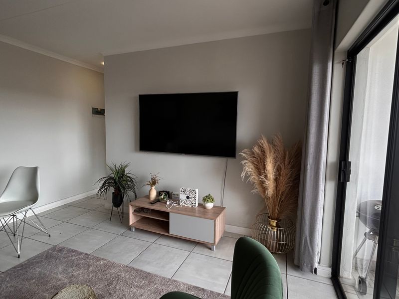 Modern open-plan living area featuring neutral tiled flooring, clean wall finishes, and a large sliding glass door providing access to the balcony.