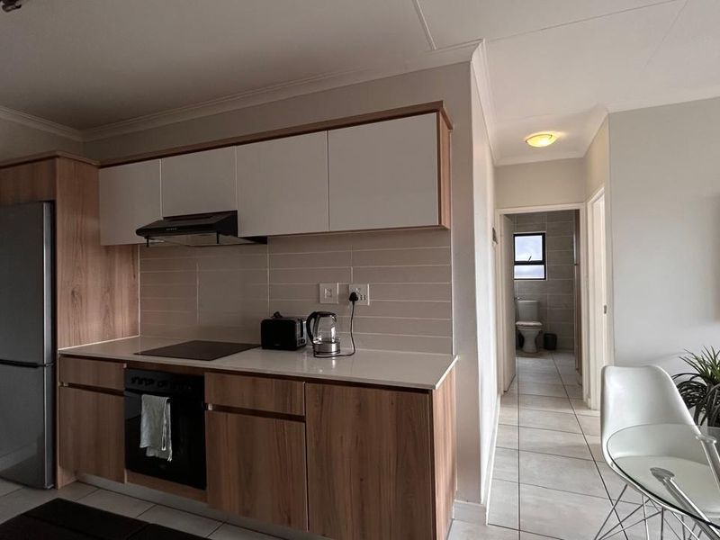 Modern open-plan kitchen featuring wood-finish cabinetry, integrated appliances, and tiled flooring, with a clear view leading toward the bathroom area.