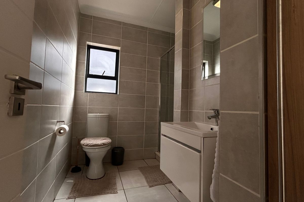 Modern bathroom featuring neutral wall and floor tiles, a sleek vanity unit with integrated basin, and a glass-enclosed shower.