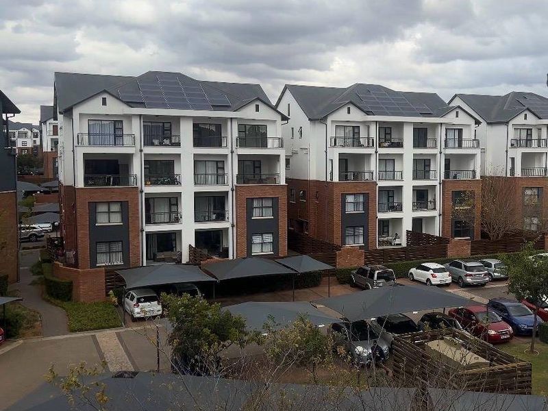 Exterior view of a modern multi-story apartment complex featuring brick and plaster facades, private balconies, and covered carport parking areas.