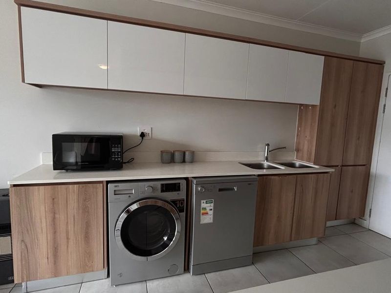 Modern kitchen featuring sleek wood-tone and white cabinetry, stone countertops, a double sink, and integrated space for laundry and dishwashing appliances.