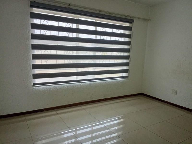 An empty bedroom featuring neutral tiled flooring, textured walls, and modern zebra blinds, providing a clean and versatile space ready for personalization.