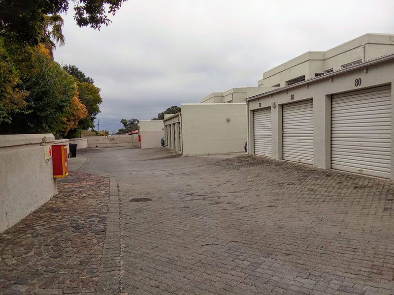 Exterior view of a row of residential garages with roller shutter doors and a paved driveway area.