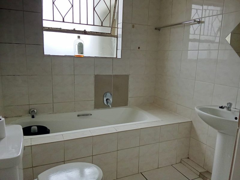A functional bathroom featuring a built-in bathtub, pedestal basin, and toilet, finished with neutral wall and floor tiles.