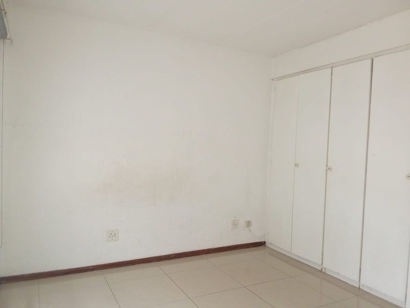 An empty bedroom featuring tiled flooring and built-in cupboards, requiring minor cosmetic updates to the wall finishes.