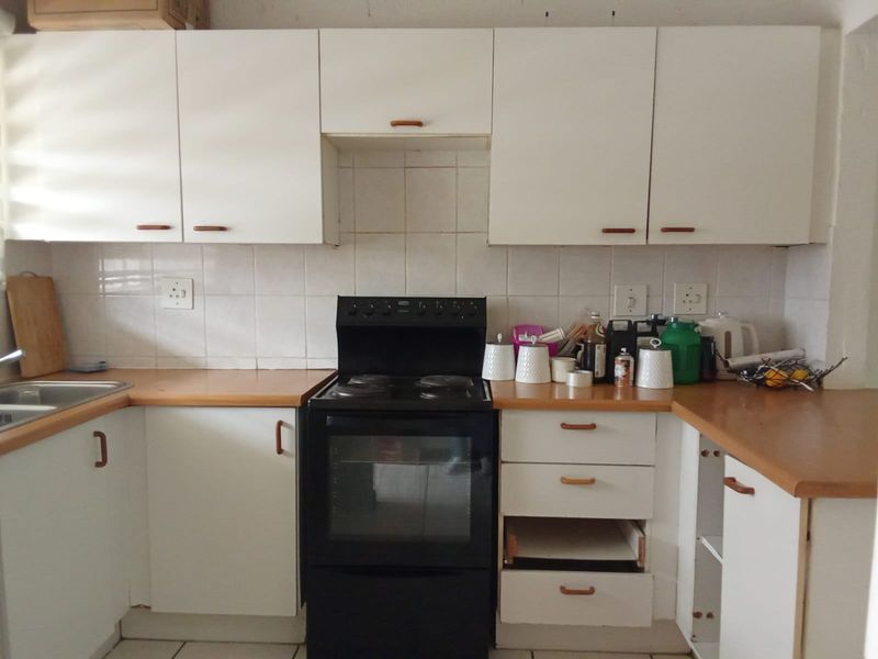 A functional kitchen featuring white cabinetry, laminate countertops, tiled backsplash, and a freestanding stove, requiring minor repairs and cosmetic updates.