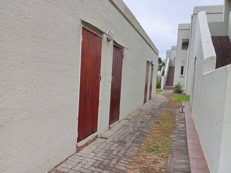A paved exterior walkway between apartment building blocks featuring multiple timber access doors and exterior wall lighting.