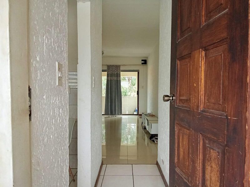 A view through a timber entrance door into a tiled hallway leading towards an open-plan living area with a sliding glass door.