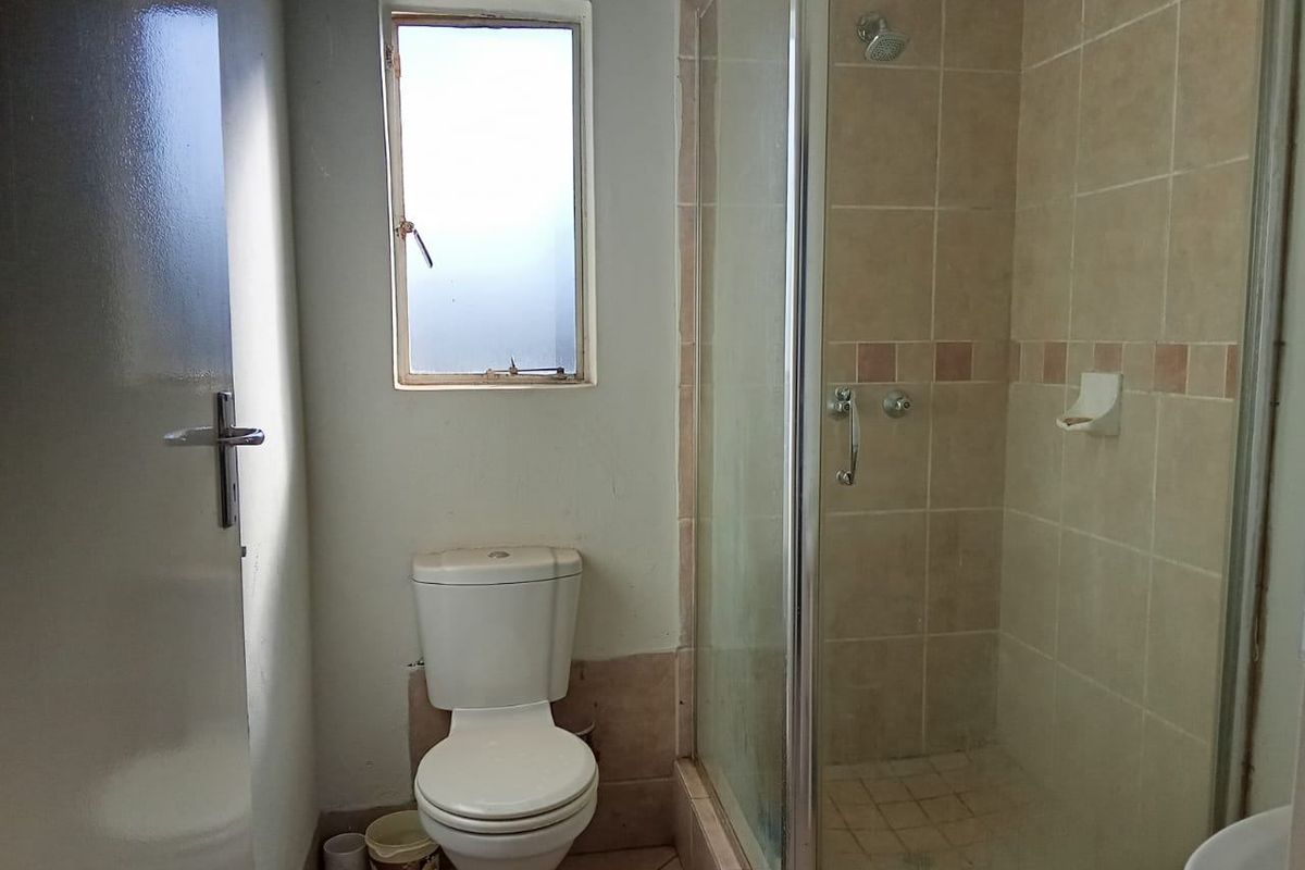 A functional bathroom featuring a shower enclosure, toilet, and tiled finishes. The space is ready for a modern update to improve its overall condition.