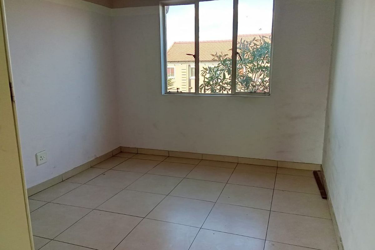 An empty bedroom featuring tiled flooring and a large window, providing a blank canvas for potential interior design and renovation.