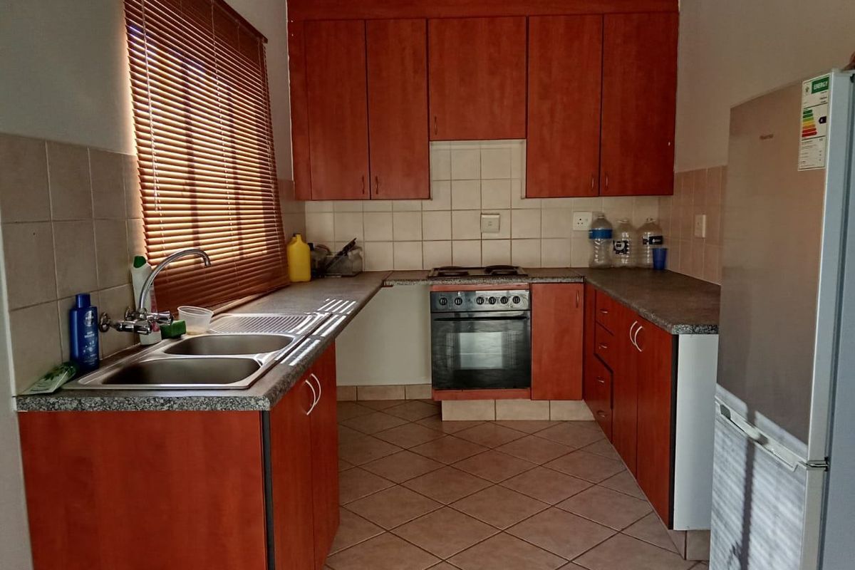 A functional kitchen featuring wood-finish cabinetry, laminate countertops, a built-in oven and hob, and tiled flooring with a neutral backsplash.