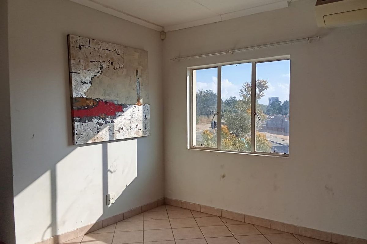 A bright, empty living area featuring ceramic tile flooring, a wall-mounted air conditioning unit, and a window with natural light.