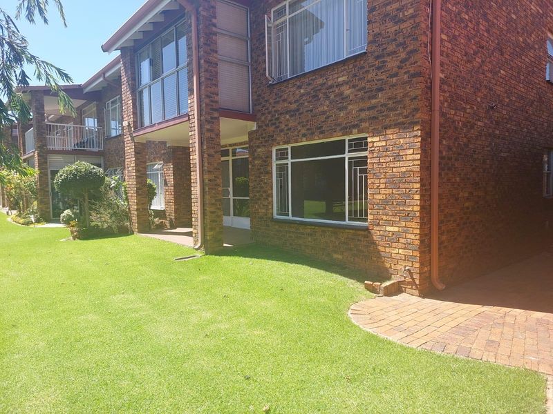 Rear view of a face brick apartment building featuring a paved patio area, balcony, and well-maintained communal garden space.