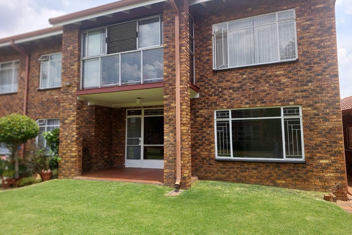 Rear view of a double-storey apartment building featuring a face brick facade, a ground-floor patio, and an upper-level balcony overlooking a private lawn.