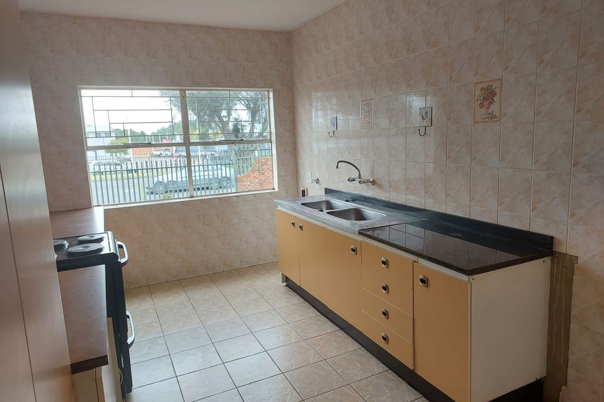 A functional kitchen featuring tiled walls, built-in cabinetry, a double bowl sink, and ceramic floor tiles, offering a blank canvas for renovation.