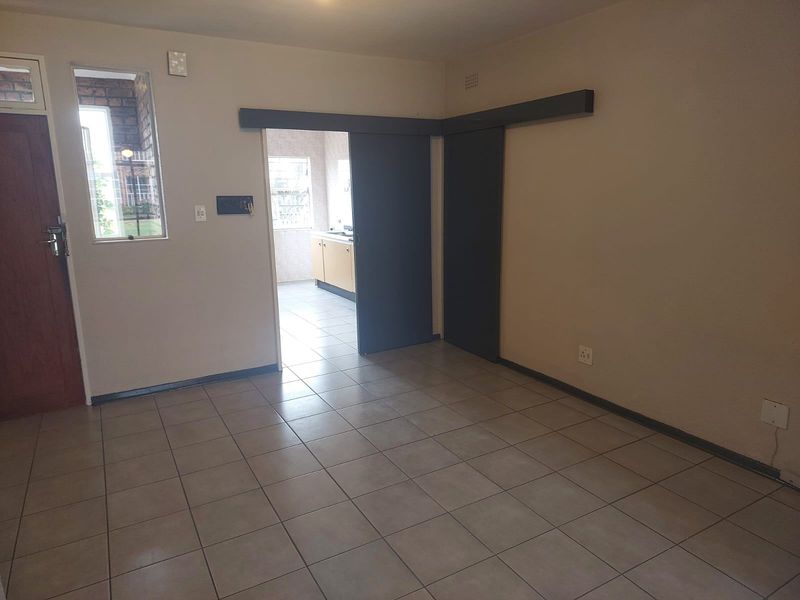 An empty living room featuring neutral tiled flooring and a sliding door leading to the kitchen area.