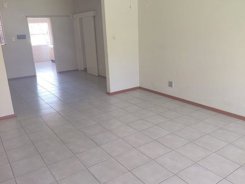 An empty, open-plan living area featuring neutral ceramic floor tiles, a ceiling fan, and clean white walls, offering a versatile blank canvas.