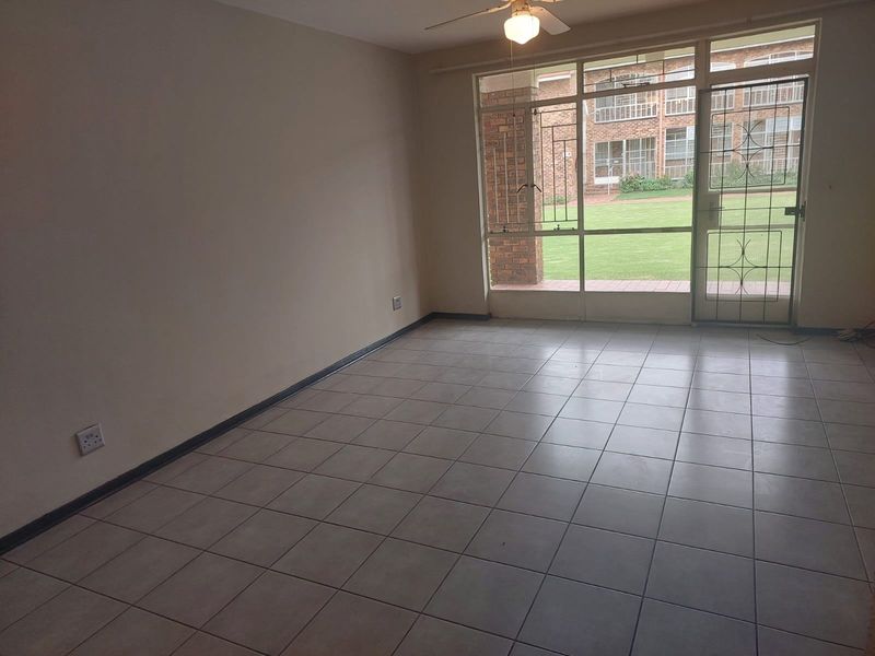 Spacious, empty living area featuring neutral tiled flooring, a ceiling fan, and large glass doors providing direct access to the garden.