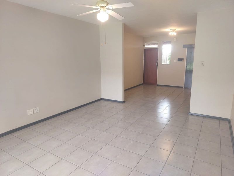 An open-plan living area featuring neutral tiled flooring, a ceiling fan, and clean wall finishes, providing a versatile space ready for personalization.