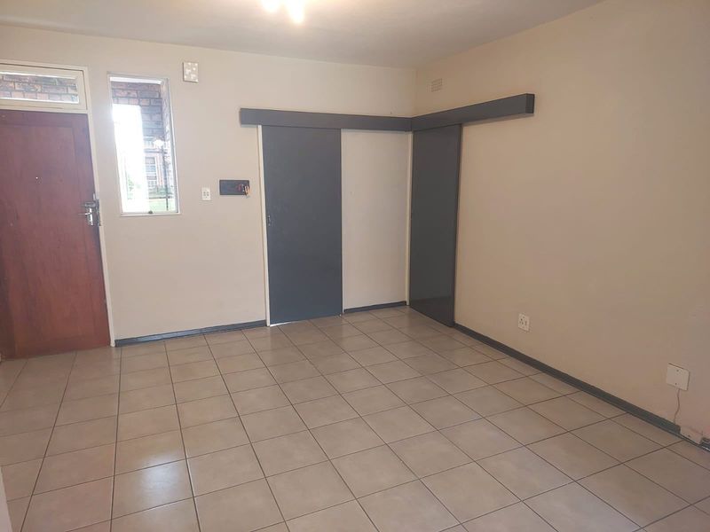 An empty living area featuring neutral tiled flooring, sliding doors, and a timber entrance door, providing a blank canvas for interior design.