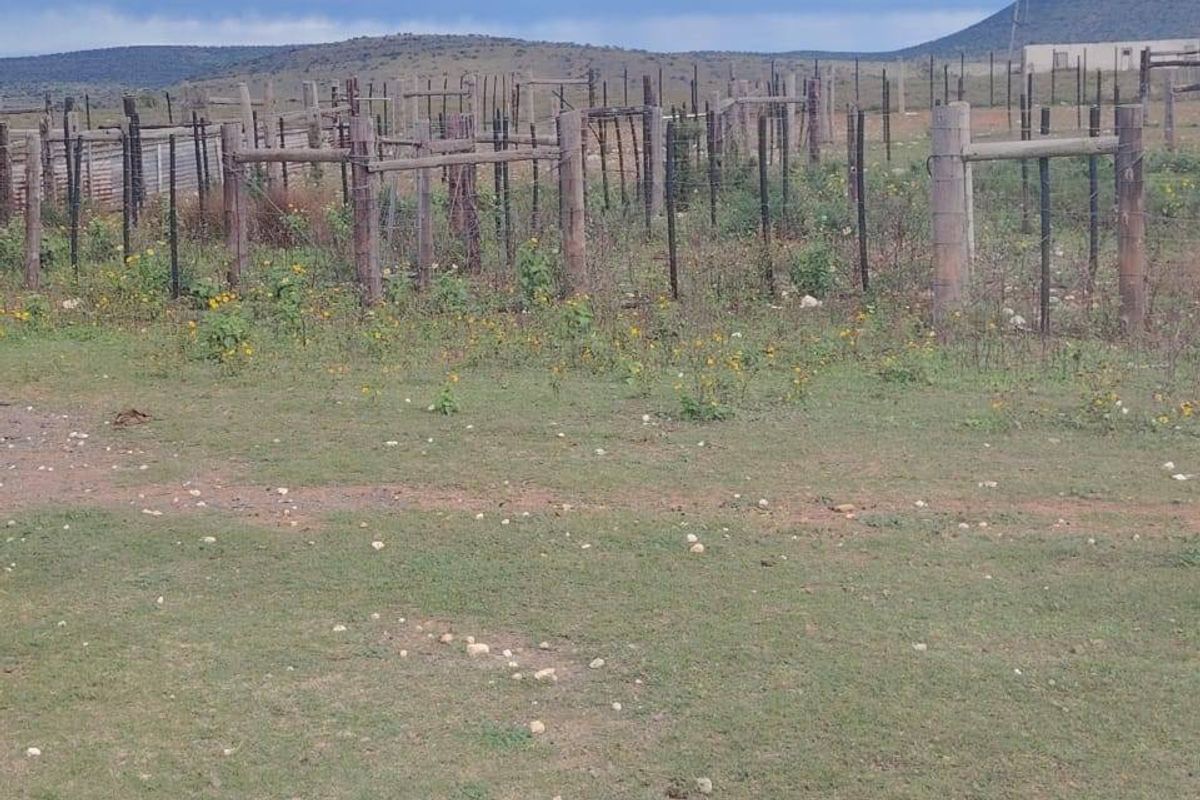 An expansive rural farm landscape featuring weathered wooden fence posts and wire fencing set against a backdrop of rolling hills and open pasture.
