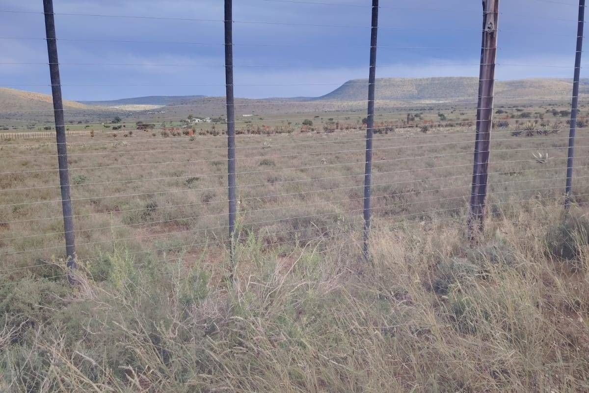 A wide-angle view of the expansive farm landscape, featuring wire perimeter fencing and distant rolling hills under a cloudy sky.