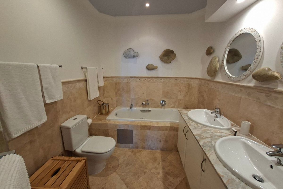 A well-maintained bathroom featuring a built-in bathtub, double vanity with stone countertops, and neutral stone tile finishes throughout.